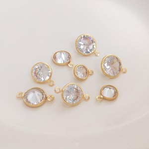 Puede incluir: Una colección de abalorios de metal dorado con brillantes redondos transparentes engastados. Cada abalorio tiene un bucle para sujetarlo a joyas u otras manualidades.