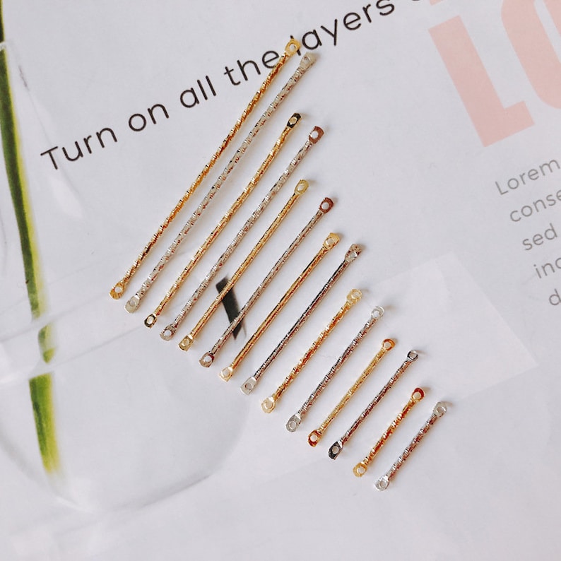 May include: A set of 10 gold and silver jump rings with textured surfaces. The jump rings are arranged in order of size, with the smallest ring at the top and the largest ring at the bottom.