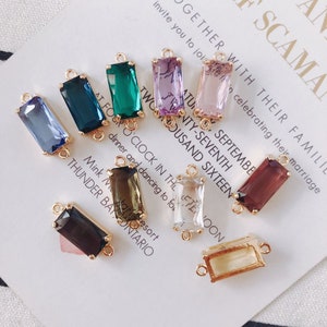 May include: Assortment of ten colorful rectangular glass charms with gold metal connector loops. The charms are in various colors including purple, pink, green, brown, clear, and blue.