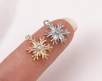 May include: Two snowflake charms, one gold and one silver, with clear crystal accents. The charms are on a finger.