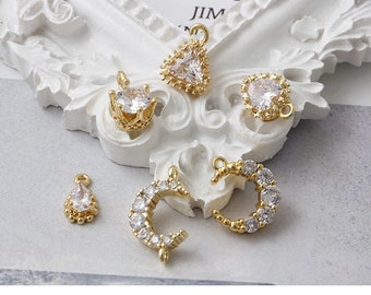 May include: Assortment of gold-tone jewelry charms featuring clear crystal accents. The charms include a crescent moon, a crown, a heart, and a teardrop.