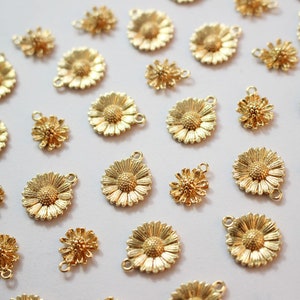 Pode incluir: Uma coleção de pingentes de metal dourado em forma de margaridas e flores menores. Os pingentes têm um laço na parte superior para prender a joias ou outros artesanatos.