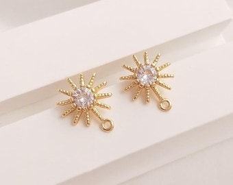 May include: A pair of gold-tone earring charms featuring a starburst design with a clear rhinestone in the center. Each charm has a small loop for attaching to jewelry.