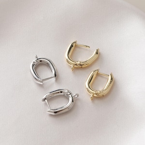 May include: Two pairs of hoop earrings, one pair is gold and the other is silver. The earrings are oval shaped and have a hinged closure.