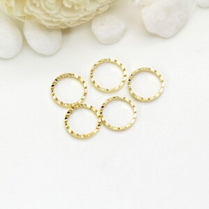May include: Five gold-colored jump rings with a textured, diamond-shaped pattern. The rings are all the same size and are arranged in a loose circle.