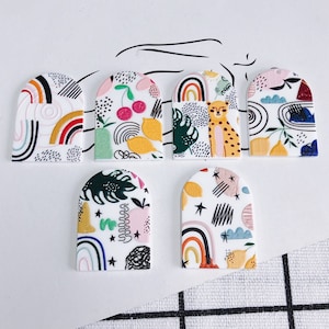 May include: Six colourful arch-shaped ceramic tiles with various patterns, including rainbows, lemons, cherries, and a leopard. The tiles are white with black outlines and are ideal for crafting projects.
