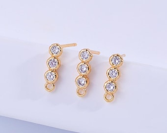 May include: Three pairs of gold-colored stud earrings. Each earring features a vertical row of four clear, round gemstones. The earrings have a post for piercing and a small loop at the bottom.