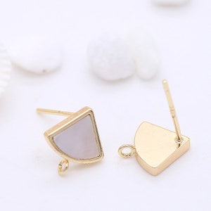 Puede incluir: Un par de hallazgos de pendientes de tono dorado con forma de semicírculo y un pequeño bucle. Los hallazgos están hechos de metal y tienen una incrustación blanca nacarada.