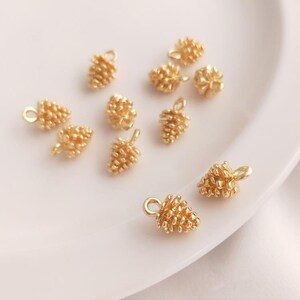 May include: A collection of ten gold-tone metal pine cone charms. The charms are small and detailed, with a textured surface that resembles a pine cone. They are perfect for adding a touch of nature to jewellery or crafts.