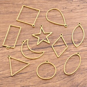 Op de afbeelding: Een verzameling van tien goudkleurige metalen hangers met open frame in diverse geometrische vormen, waaronder een vierkant, rechthoek, ster, maansikkel, driehoek, cirkel, ovaal, ruit, druppel en markies, elk voorzien van een klein oogje.