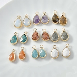 May include: Assortment of 18 gold-tone teardrop-shaped pendants with various gemstone inlays. The gemstones include amethyst, tiger's eye, turquoise, and more.