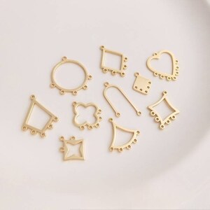 Puede incluir: Una colección de dijes de metal dorado en varias formas, incluyendo un círculo, un cuadrado, un corazón y una flor. Los dijes tienen pequeños agujeros alrededor de los bordes y están diseñados para la elaboración de joyas.
