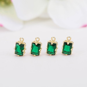 May include: Four gold-toned charms with emerald green square-shaped glass stones. Each charm has a loop at the top for attaching to jewelry.