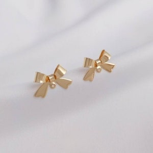 May include: A pair of gold bow-shaped earring charms with a jump ring for attaching to jewelry.