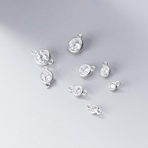 May include: A set of silver-toned jewellery connectors with clear crystal accents. The connectors are round and have a loop on each side.