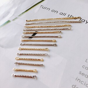 May include: A row of 10 gold and silver chain connectors with small loops at each end. The connectors are arranged in a diagonal line on a white surface.