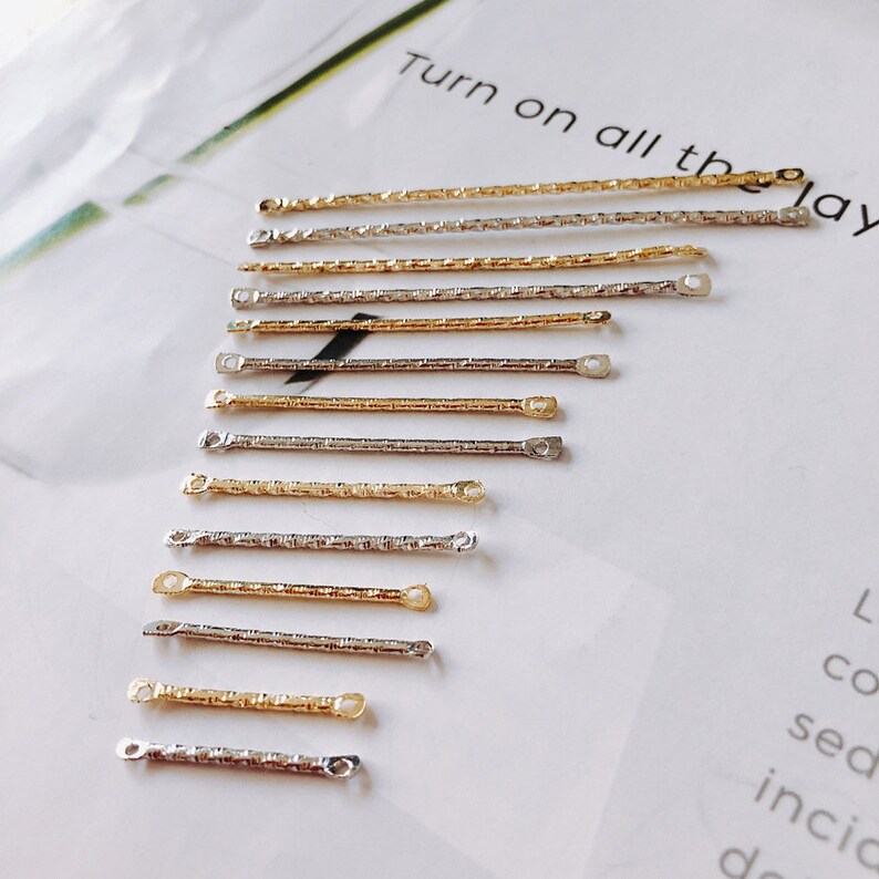 May include: A row of 10 gold and silver chain connectors with small loops at each end. The connectors are arranged in a diagonal line on a white surface.