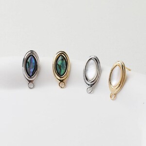 May include: Four oval-shaped earring findings with a silver, gold, and iridescent shell design. Each finding has a loop at the bottom.