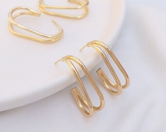 Puede incluir: Un par de pendientes de aro doble de color dorado. Los pendientes están hechos de dos alambres finos y curvos que están conectados en la parte superior e inferior. Los pendientes son un diseño simple y elegante.