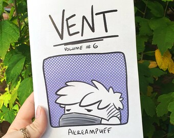 May include: A white zine titled "VENT Volume #6" featuring a cartoon illustration of a person wearing a face covering. The illustration is in a purple box with white dots. The artist's name, "AKREAMPUFF," is below the illustration.