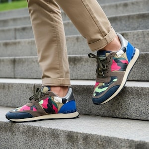 May include: Multi-colored camouflage sneakers with blue, pink, green, and brown accents. The sneakers have a navy blue sole and a silver heel. The laces are olive green. The sneakers are on a person walking down a set of concrete stairs.