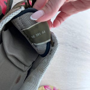 May include: Close-up of a worn sneaker interior. The shoe features a mesh lining and a label with the numbers "BE 291 44". The exterior shows a camouflage pattern with shades of green, brown, and red.