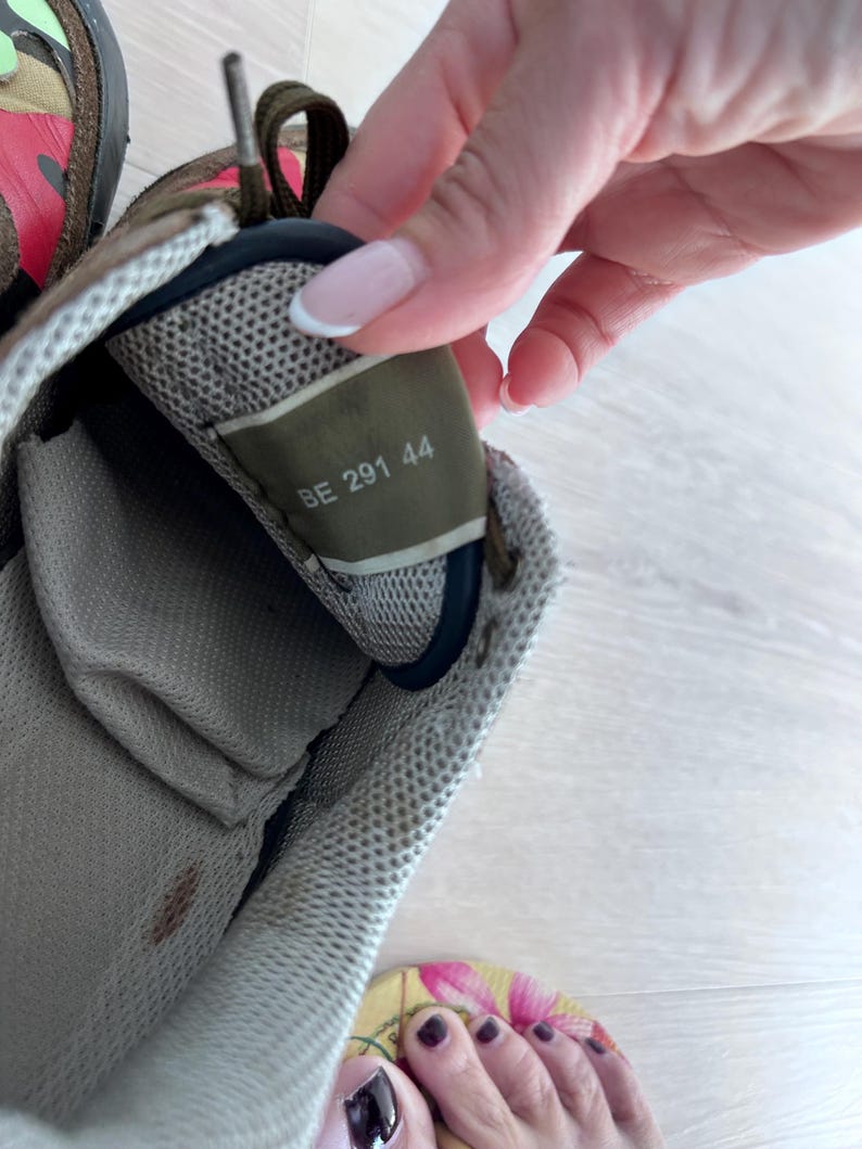 May include: Close-up of a worn sneaker interior. The shoe features a mesh lining and a label with the numbers "BE 291 44". The exterior shows a camouflage pattern with shades of green, brown, and red.