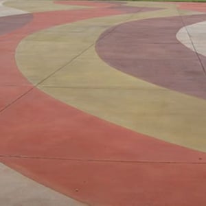 May include: A concrete floor with a design of curved lines in shades of red, brown, and yellow.