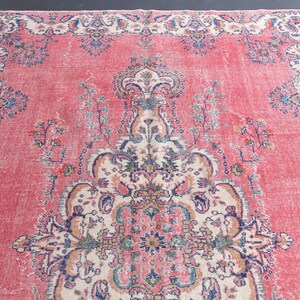K&ouml;nnte beinhalten: Ein vintagefarbener rosa Teppich mit einem floralen Muster. Der Teppich hat ein zentrales Medaillon mit komplizierten Details und einen Rand mit einem sich wiederholenden floralen Muster.