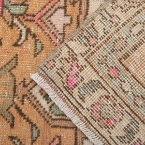 Puede incluir: Primer plano del reverso de una alfombra vintage con un patr&oacute;n geom&eacute;trico marr&oacute;n, beige y rosa. La alfombra tiene un borde de flecos.