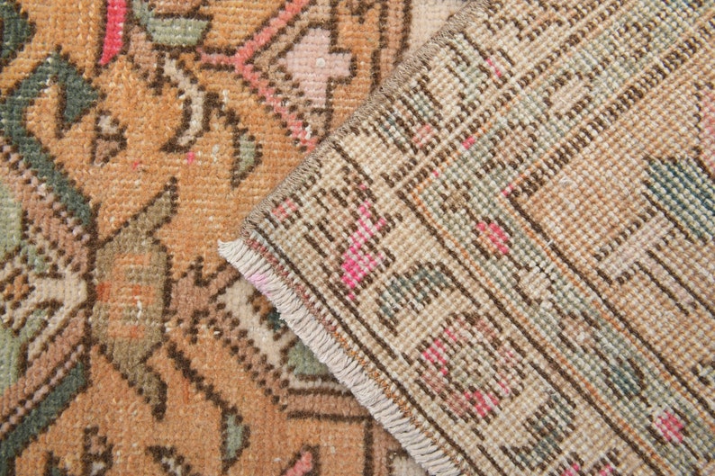Puede incluir: Primer plano del reverso de una alfombra vintage con un patr&oacute;n geom&eacute;trico marr&oacute;n, beige y rosa. La alfombra tiene un borde de flecos.