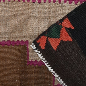 May include: Close-up of a brown, black and pink woven rug with a geometric pattern. The rug has a fringed border.