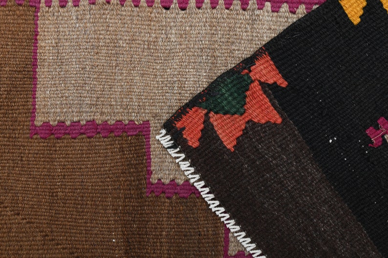 May include: Close-up of a brown, black and pink woven rug with a geometric pattern. The rug has a fringed border.