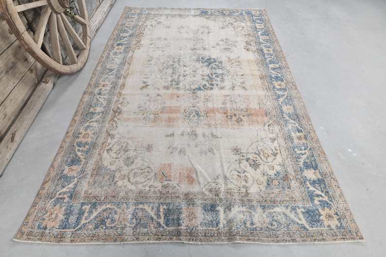 May include: A vintage rug with a cream background and a blue and brown floral pattern. The rug has a distressed look and is perfect for adding a touch of bohemian style to your home.