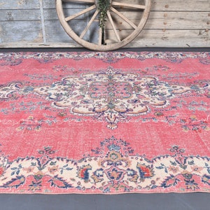 K&ouml;nnte beinhalten: Ein vintagefarbener rosa Teppich mit einem floralen Muster und einem zentralen Medaillon. Der Teppich hat einen verblassten, abgenutzten Look, der ihm einen einzigartigen Charakter verleiht.
