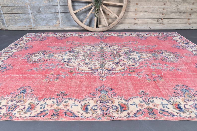 K&ouml;nnte beinhalten: Ein vintagefarbener rosa Teppich mit einem floralen Muster und einem zentralen Medaillon. Der Teppich hat einen verblassten, abgenutzten Look, der ihm einen einzigartigen Charakter verleiht.
