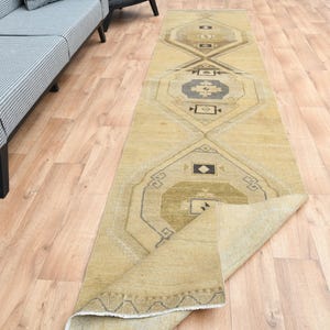 May include: A beige and brown patterned runner rug with a geometric design. The rug is folded in half and is lying on a wooden floor.