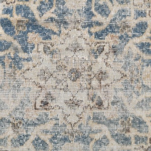 May include: A vintage rug with a faded blue and cream floral pattern. The rug has a distressed look and is made of a woven material.