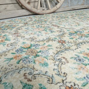 May include: A vintage cream-colored rug with a floral pattern in shades of blue, green, and orange. The rug has a distressed look, with some areas faded and worn.