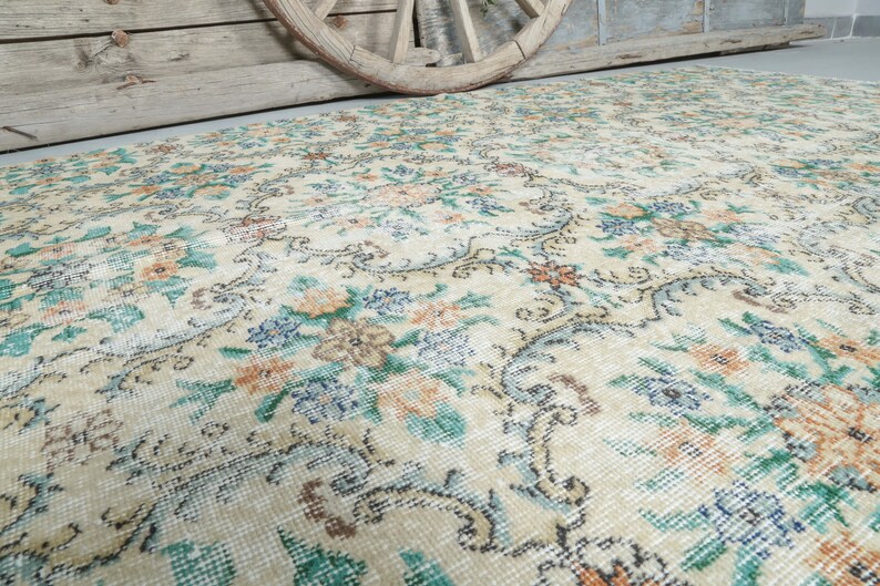 May include: A vintage cream-colored rug with a floral pattern in shades of blue, green, and orange. The rug has a distressed look, with some areas faded and worn.
