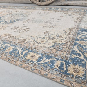 May include: A vintage rug with a cream background and a blue and beige floral pattern. The rug has a distressed look and is perfect for adding a touch of bohemian style to any room.