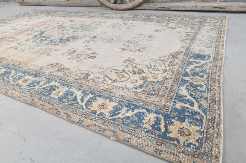 May include: A vintage rug with a cream background and a blue and beige floral pattern. The rug has a distressed look and is perfect for adding a touch of bohemian style to any room.
