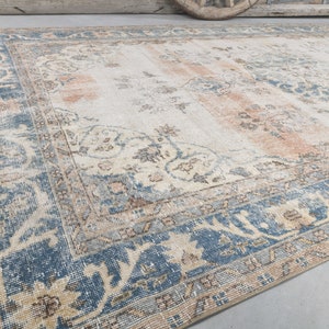 May include: A vintage rug with a cream background and a blue and beige patterned border. The rug has a faded, distressed look.