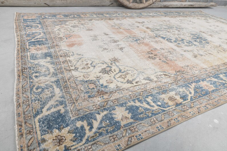 May include: A vintage rug with a cream background and a blue and beige patterned border. The rug has a faded, distressed look.