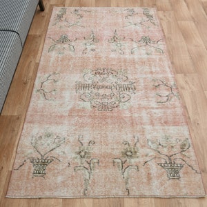 Puede incluir: Una alfombra vintage con un fondo rosa descolorido y un patrón floral en tonos marrones y verdes. La alfombra tiene un aspecto desgastado y es perfecta para añadir un toque de estilo bohemio a cualquier habitación.
