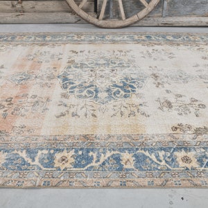 May include: A vintage rug with a cream background and a blue and beige floral pattern. The rug has a faded look and a distressed border.