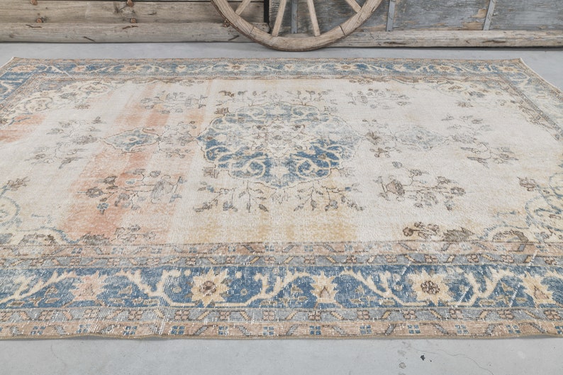 May include: A vintage rug with a cream background and a blue and beige floral pattern. The rug has a faded look and a distressed border.