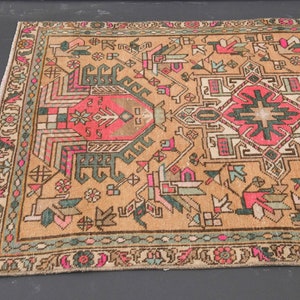 Puede incluir: Una alfombra turca vintage con fondo beige y intrincados patrones geom&eacute;tricos en tonos rosa, verde y marr&oacute;n. La alfombra tiene un borde con flecos.