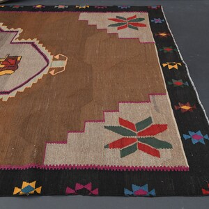 May include: A brown and beige rug with a colourful geometric pattern. The rug has a black border with colourful accents.