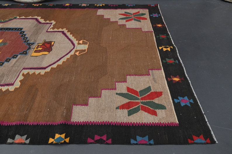 May include: A brown and beige rug with a colourful geometric pattern. The rug has a black border with colourful accents.